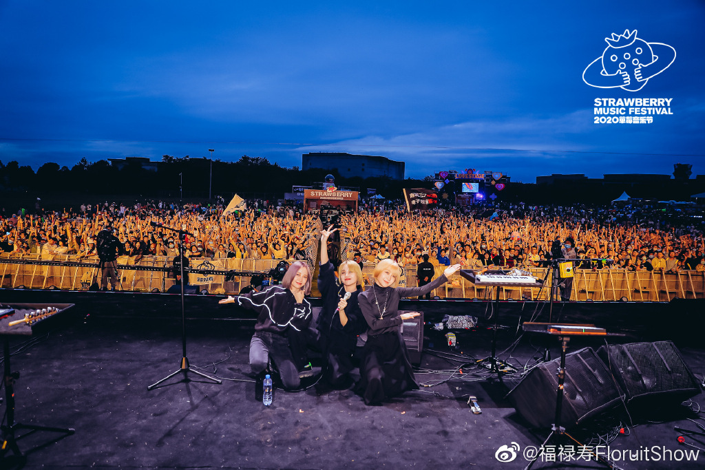 2020 年草莓音乐节舞台上的三位成员向观众比出手势，台下是密集的人海