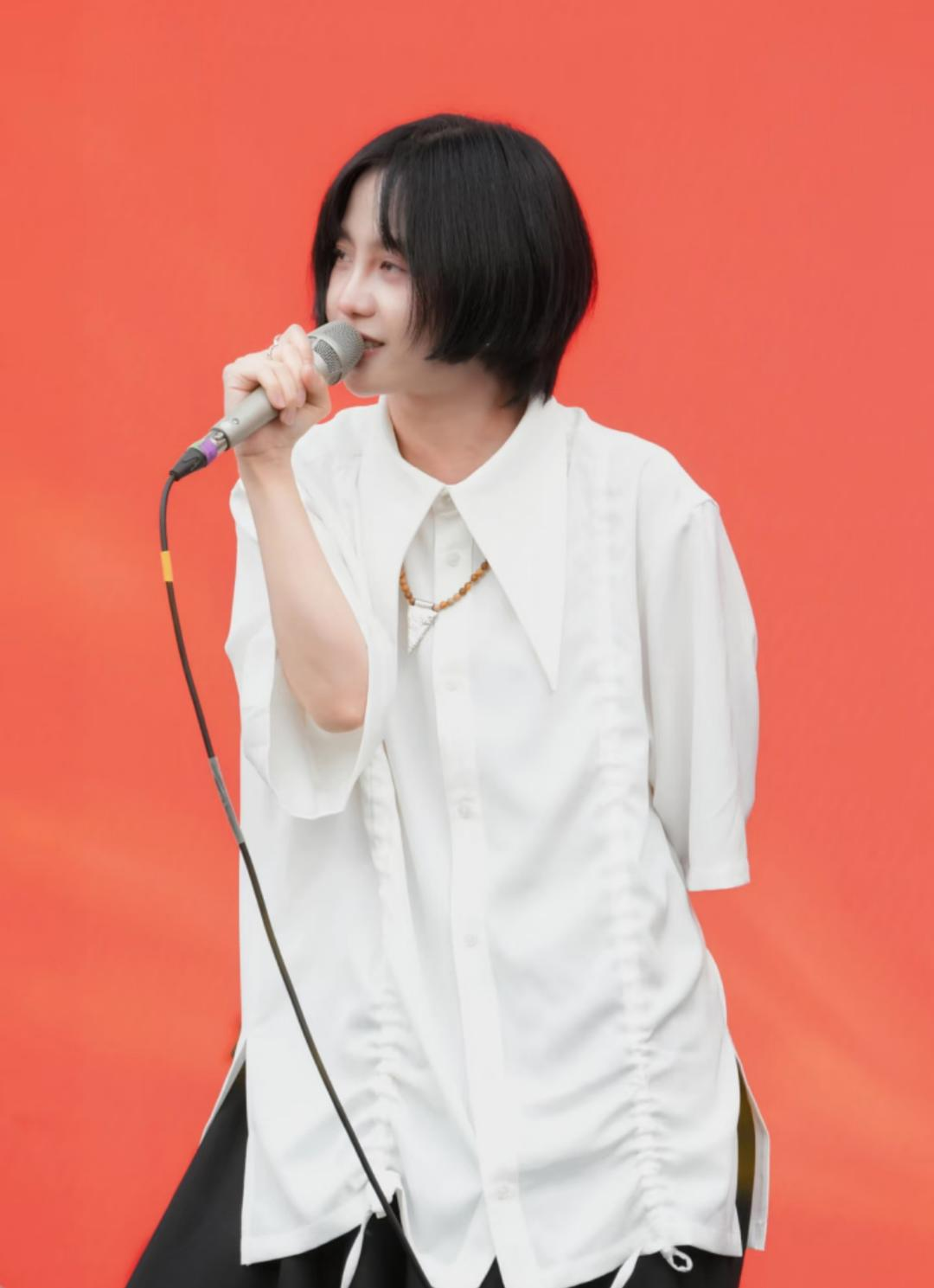 成员手持话筒演唱，身着白色大尖领衬衫，背景为纯色暖橙红