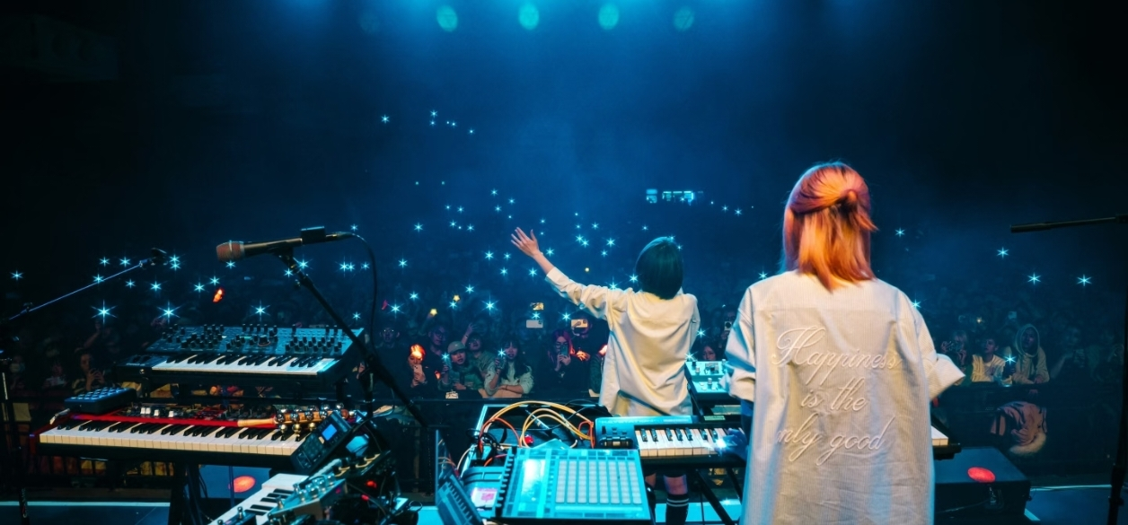 从舞台侧后方拍摄的 livehouse 现场，台下是举着手机的观众